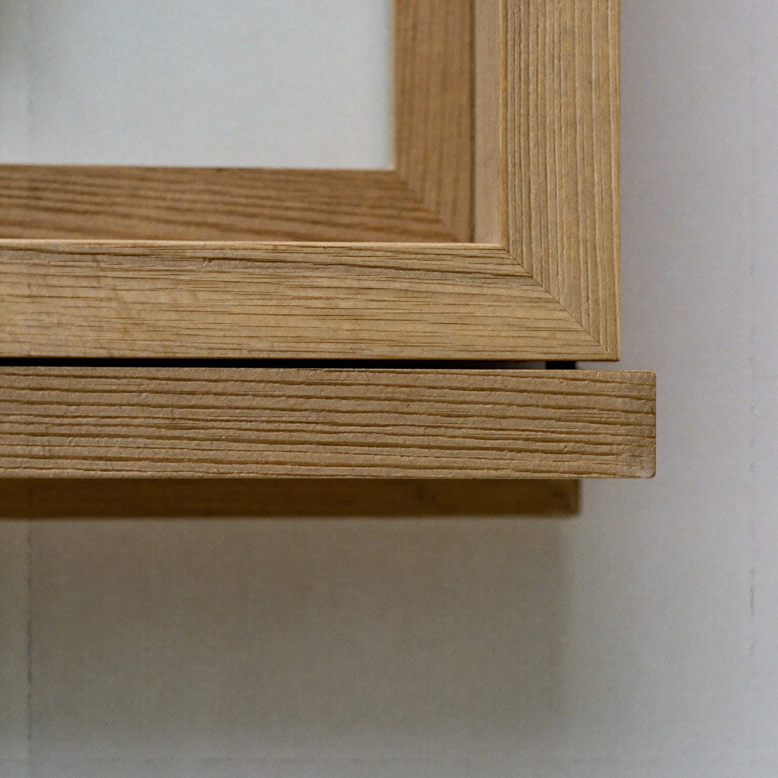 Macro detail of the mitred corner of a solid oak frame against a white wall.