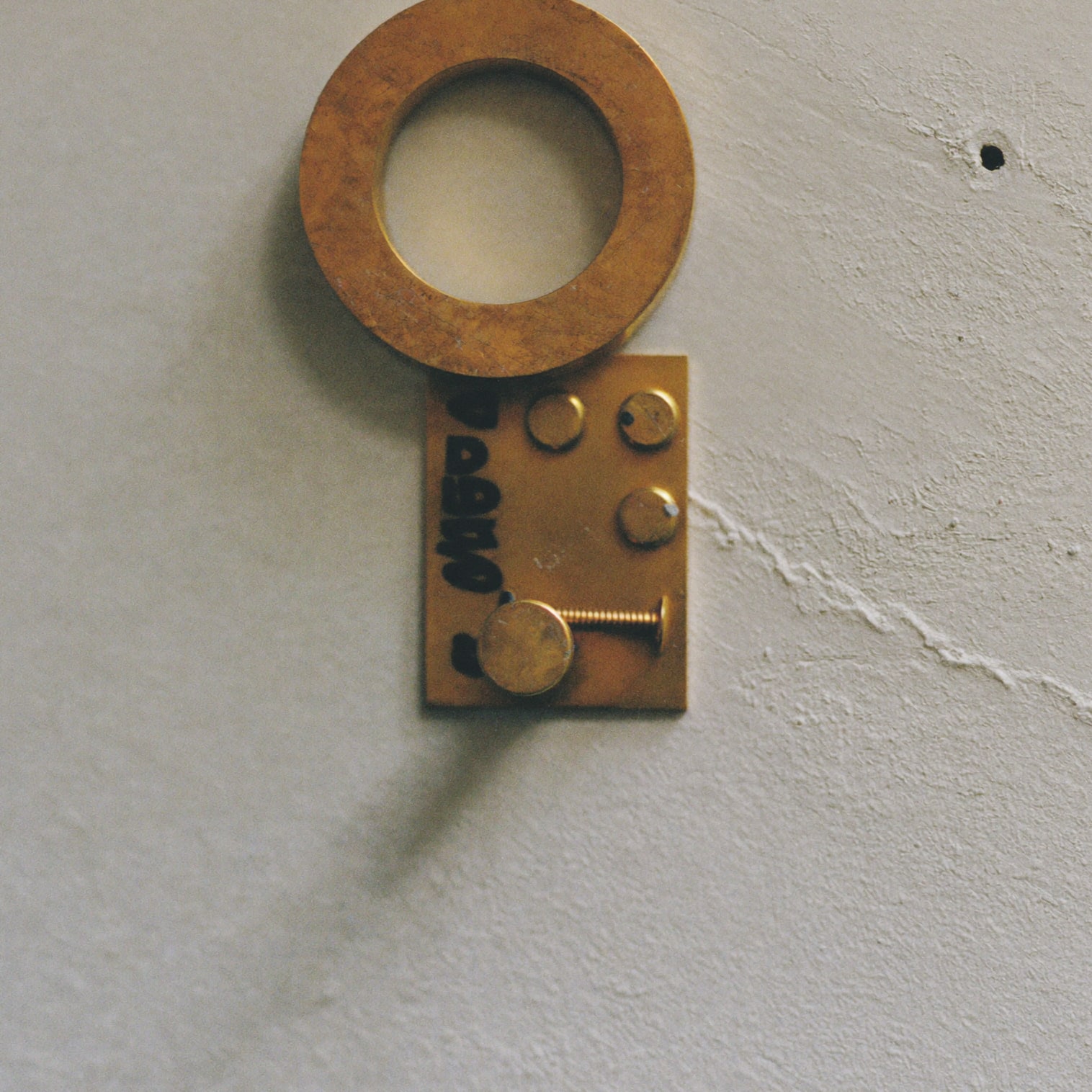 Macro detail of a solid brass picture hook and three brass screws on plaster.