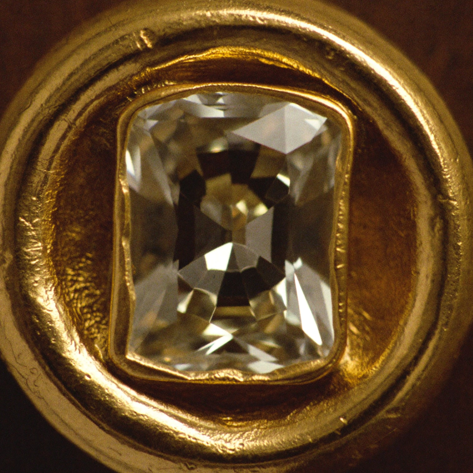 Macro detail of an uncut stone held by burnished gold foil pressed around its edge.