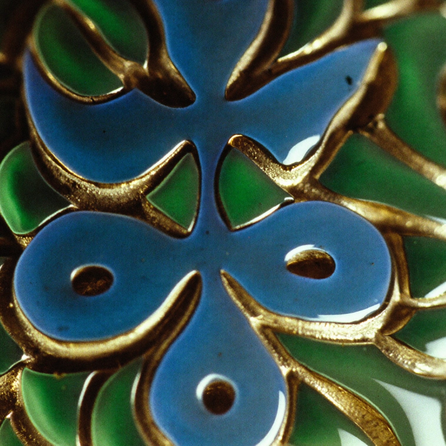 Macro detail of green and blue vitreous enamel fired into engraved gold channels.