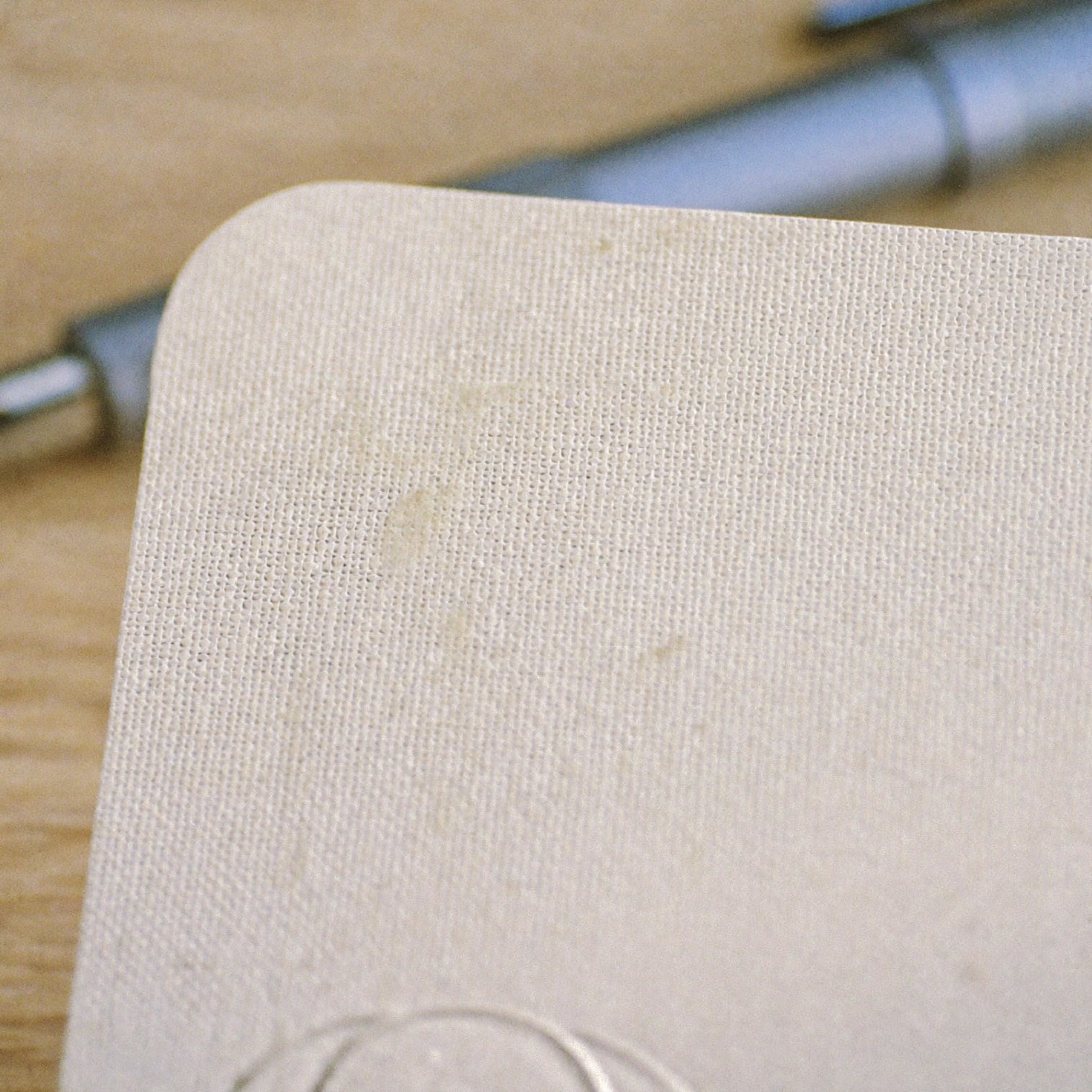 Macro detail of the deckled edge of a cotton-rag certificate card on pale oak.