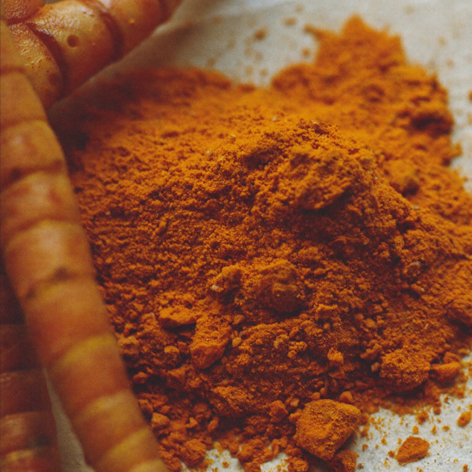 Macro detail of dried turmeric fingers beside stone-ground powder.